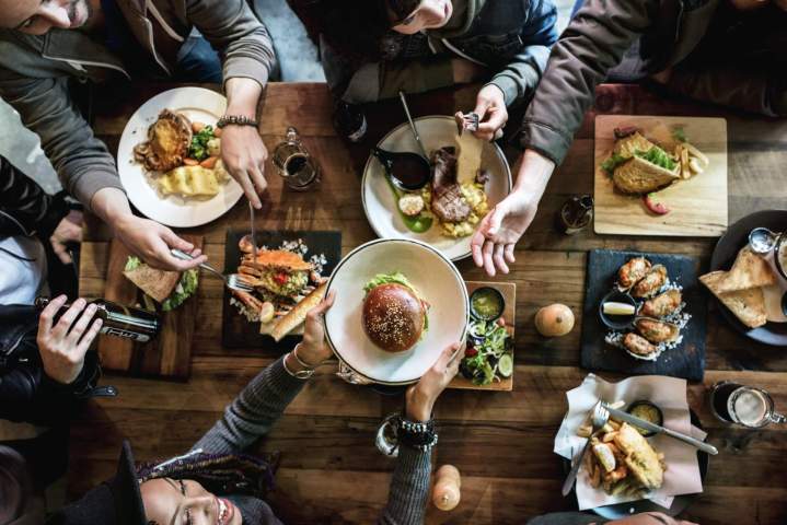 Ambiance conviviale et chaleureuse dans une salle de restaurant, avec des groupes de personnes discutant et déjeunant.